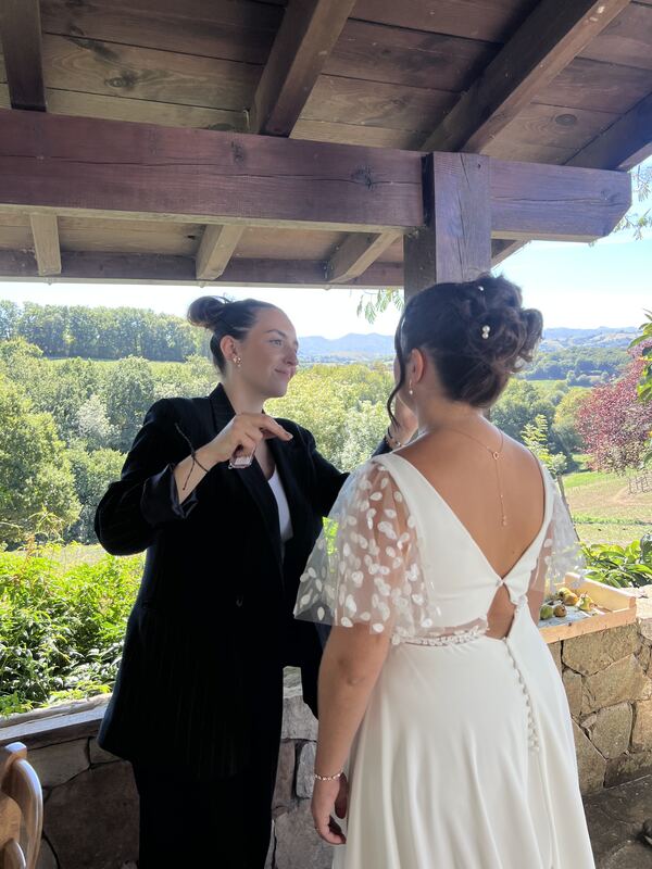 Dernières retouches sur une mariée, sur une terrasse face à la campagne.