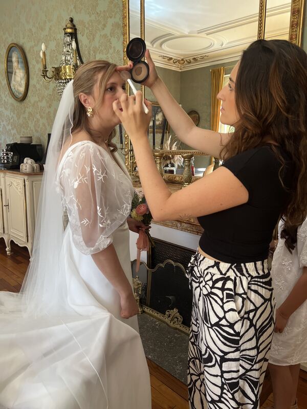 Retouche du maquillage d’une mariée voilée devant un miroir ancien.