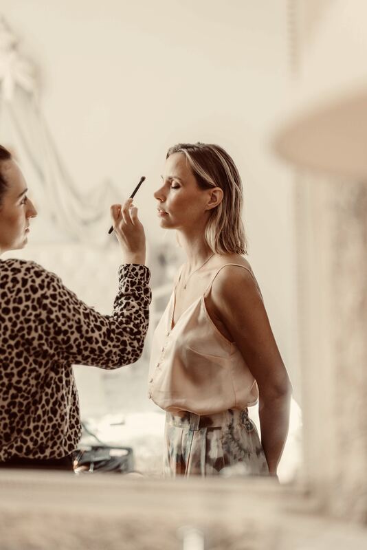 Maquillage d’une mariée près d’une fenêtre, lumière douce.