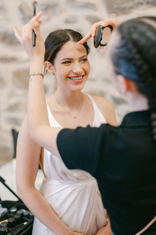 Une mariée souriante pendant sa coiffure et son maquillage.