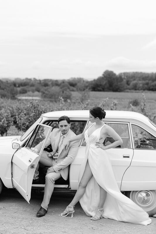 Les mariés près d’une voiture ancienne, en noir et blanc.