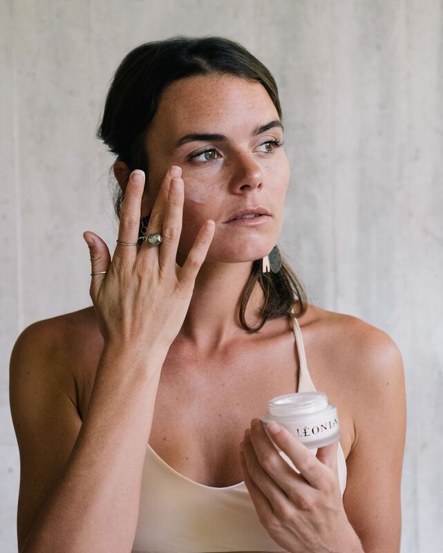 Une femme applique une crème Léonia sur son visage.